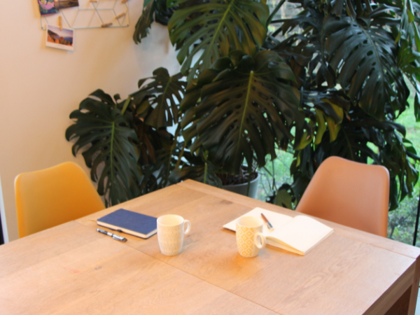 Een tafel met twee stoelen, bij elke plaats staat een mok thee en ligt er een notitieboekje met pen. Een tafel met twee stoelen, bij elke plaats staat een mok thee en ligt er een notitieboekje met pen.